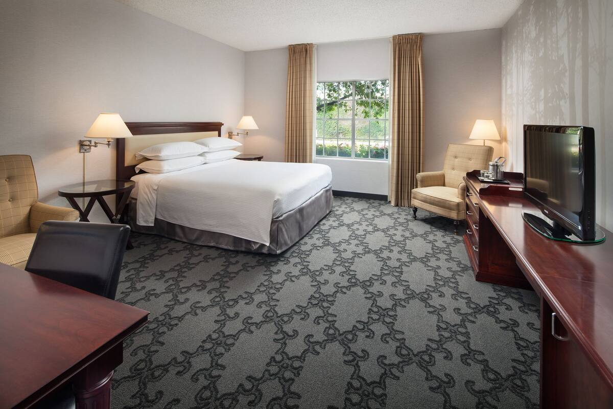 A hotel room with a bed, two bedside tables with lamps, a TV, a desk, and a chair.