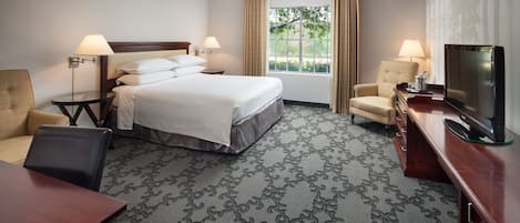 A hotel room with a bed, two bedside tables with lamps, a TV, a desk, and a chair.