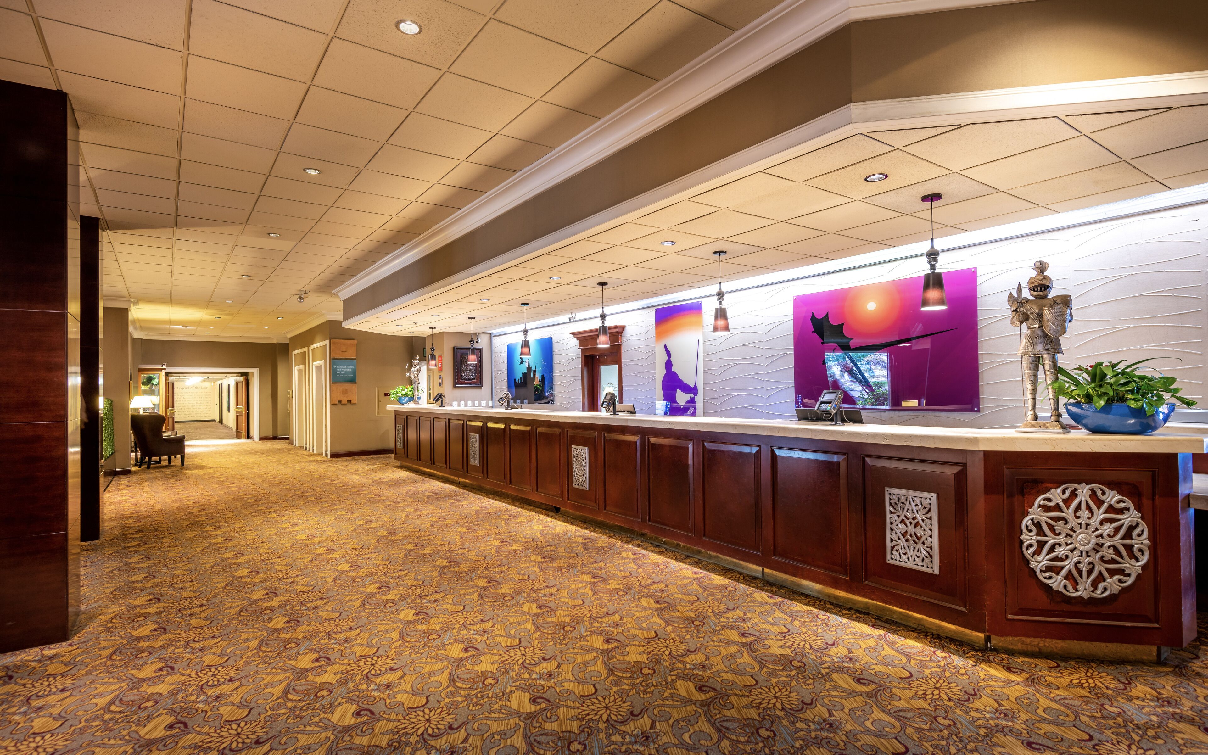 A hotel reception area with a long counter, decorative wall art, and a patterned carpet.