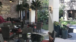 Un área de patio al aire libre con mobiliario de mimbre, una mesa con cubierta de vidrio y luces colgantes.