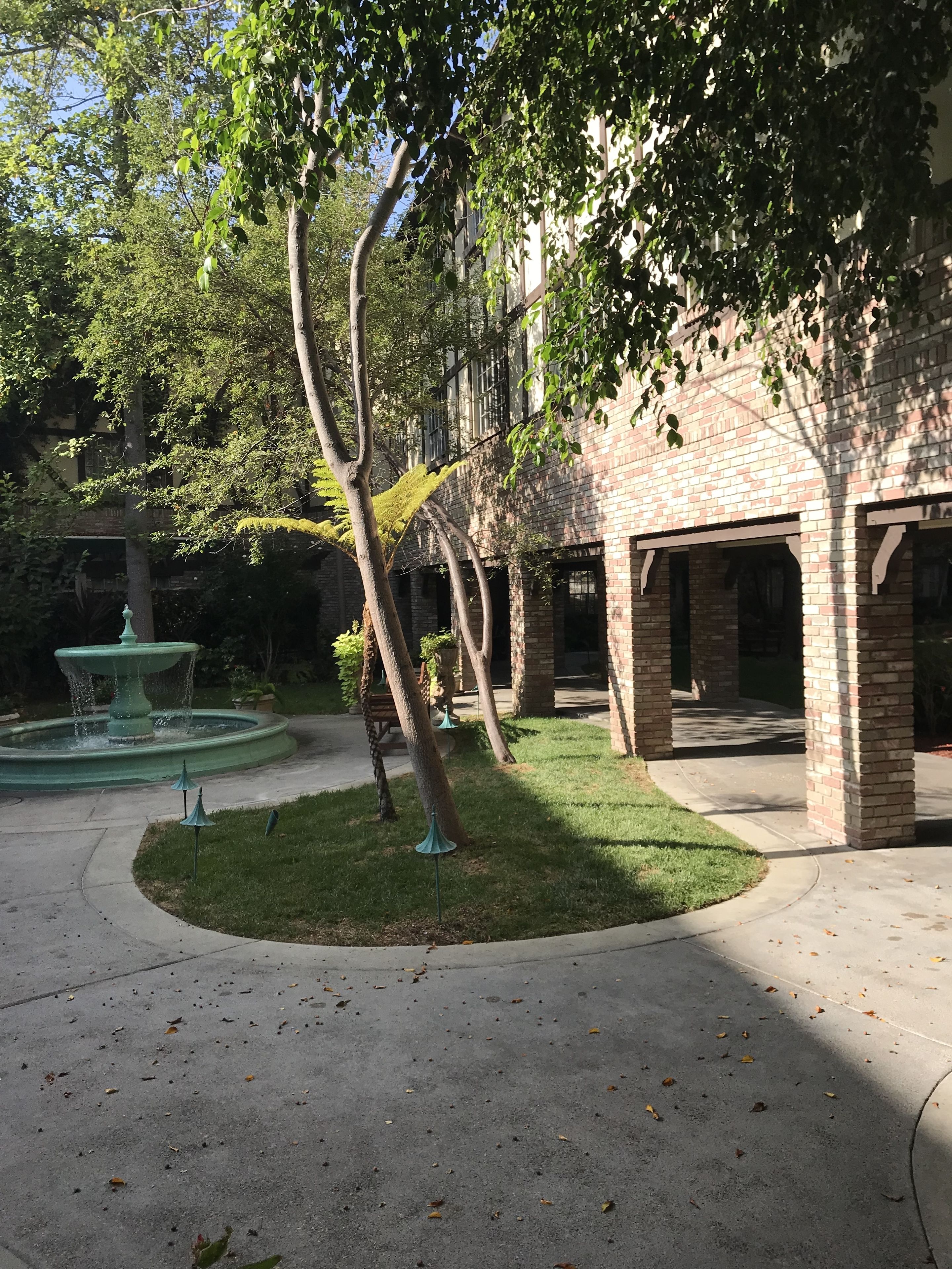 A courtyard with a fountain, brick buildings, and trees.