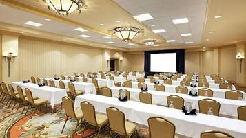 A conference room with rows of tables and chairs, a large screen, and chandeliers.