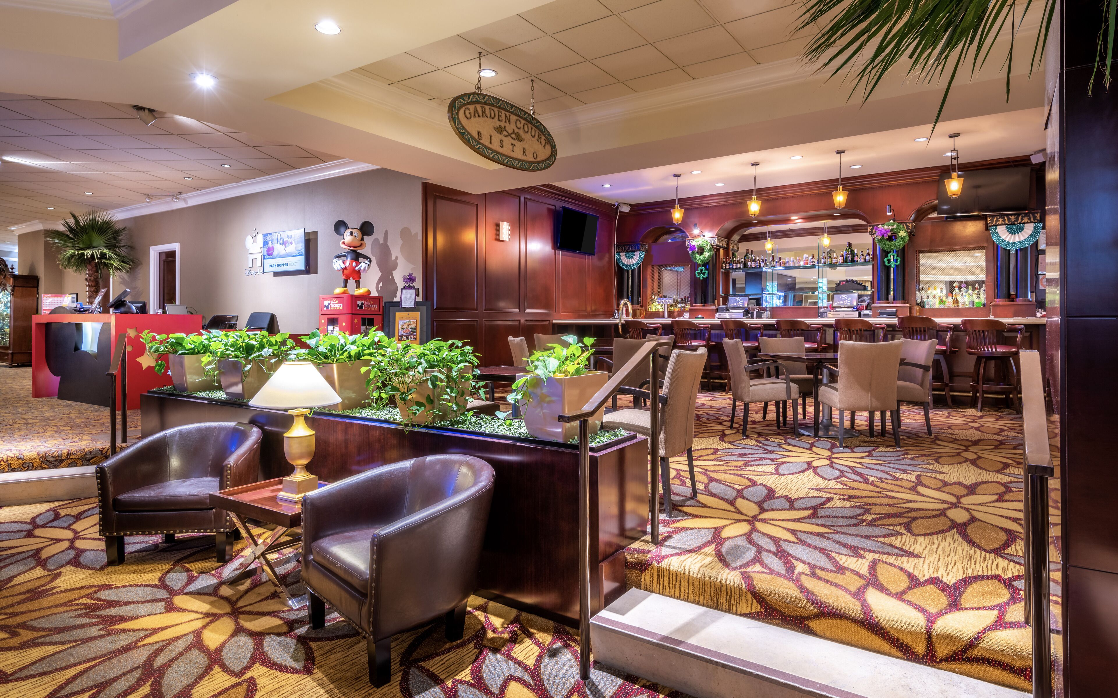 Una hall d'albergo con reception, posti a sedere confortevoli, un'area bar e un'imponente statua di Topolino.