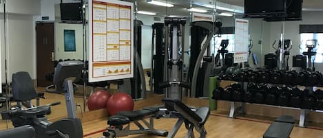 A gym with exercise equipment, a mirror, and a wall with informational posters.