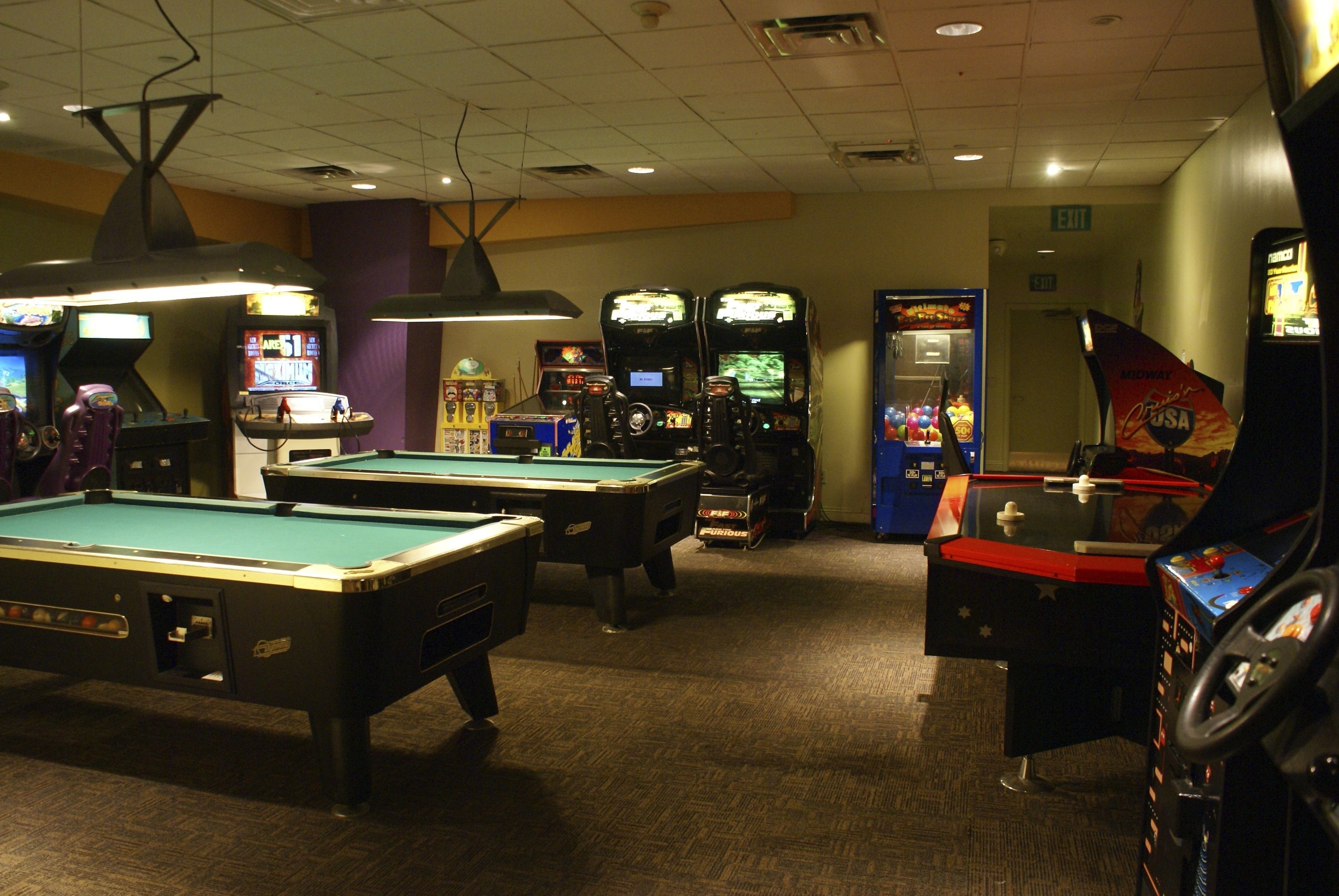 A pool table, arcade machines, and a billiards table in a room with carpeted flooring and overhead lighting.
