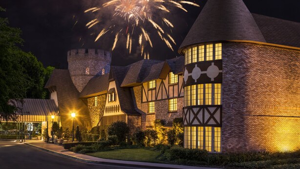 Un edificio con aspecto de castillo, con una torre, ventanas iluminadas y una característica acuática similar a un foso.
