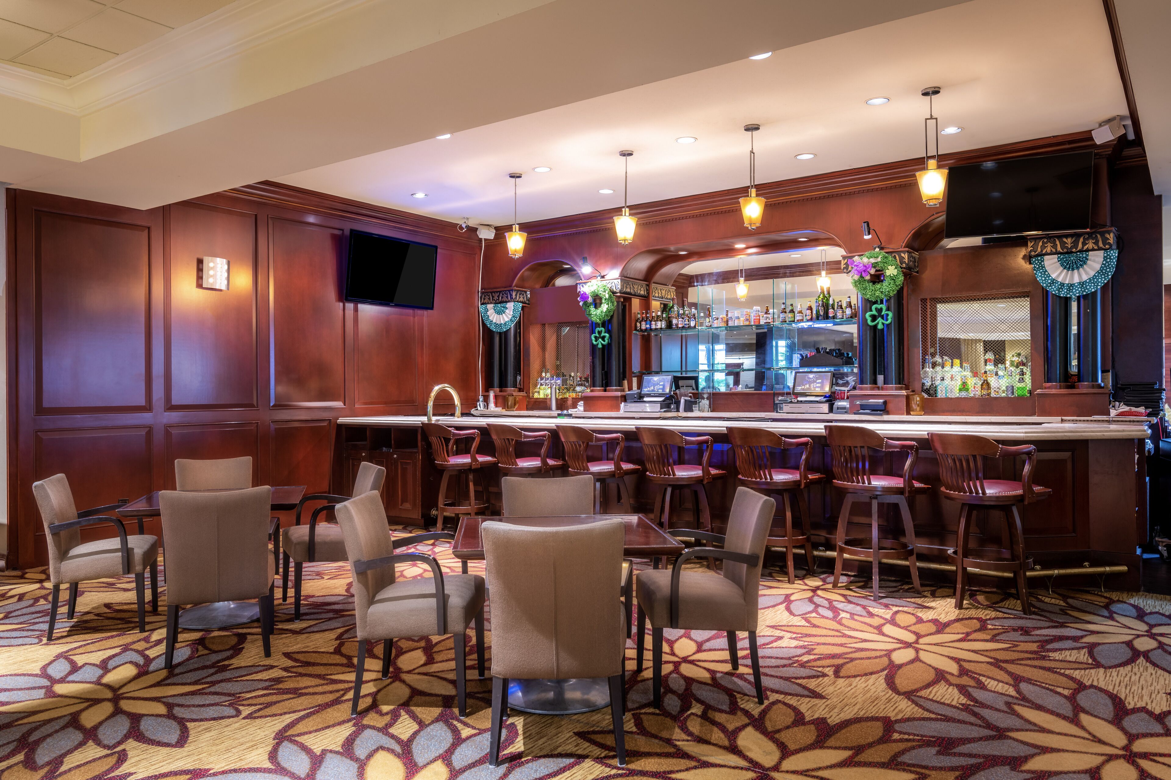 A bar area with multiple seating options, a counter with a bar, and a television mounted on the wall.