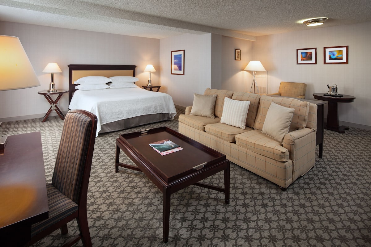 A hotel room with a bed, a sofa, a coffee table, a desk, and lamps.