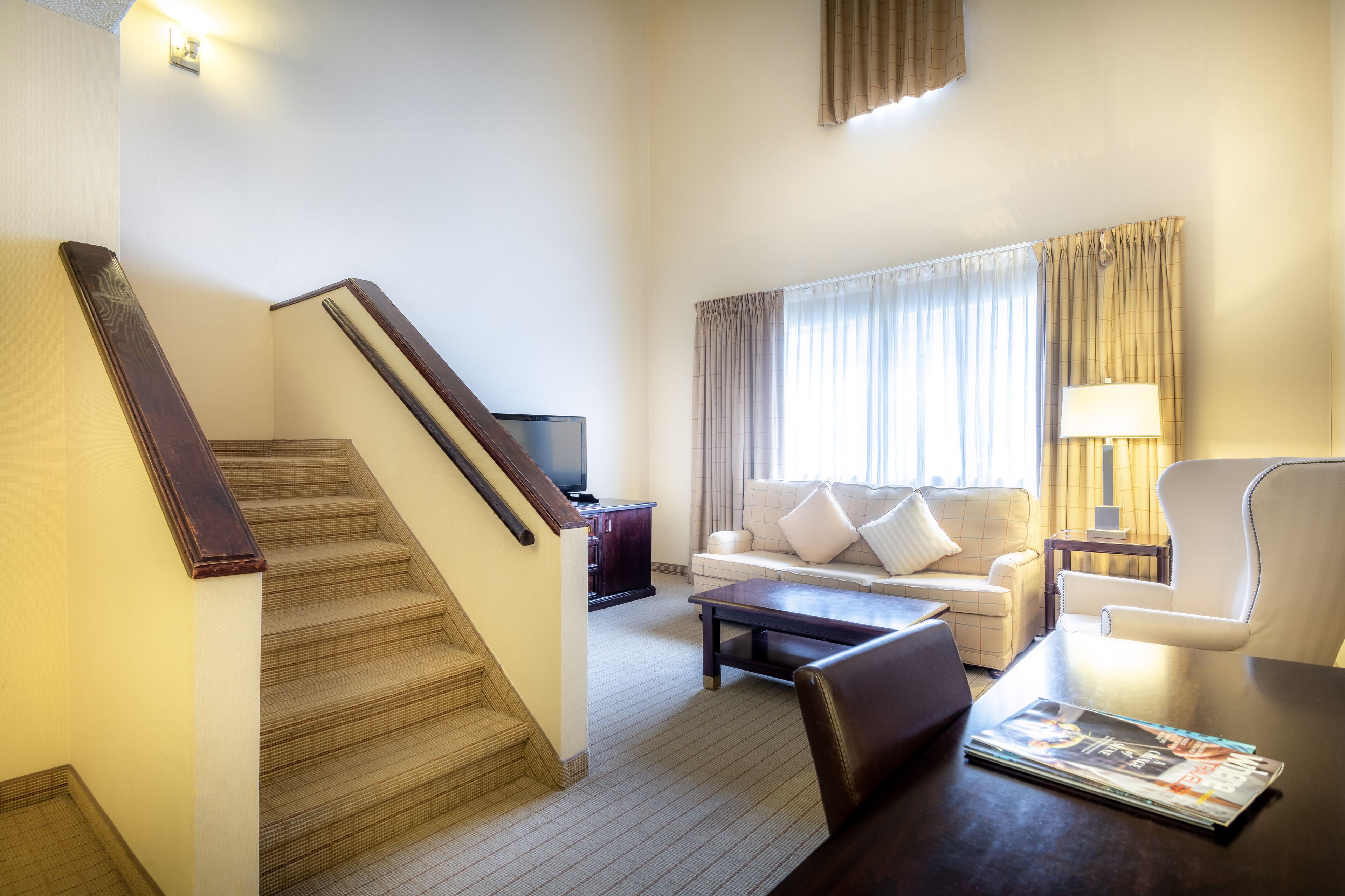 A hotel room with a staircase, a sofa, a coffee table, and a lamp.