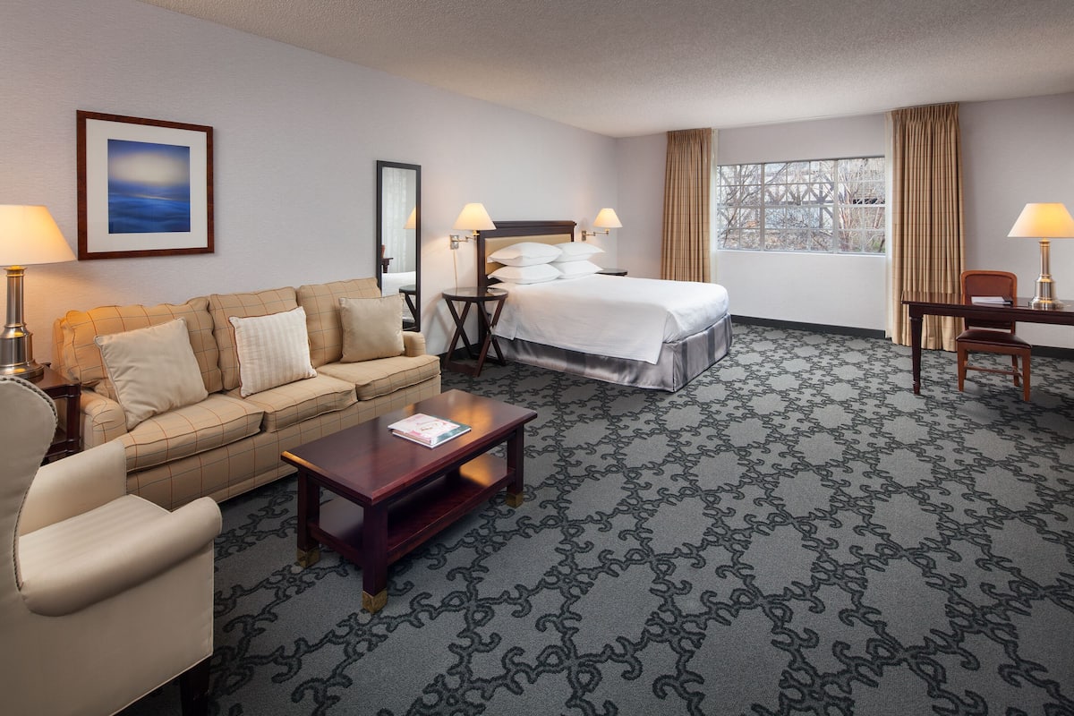 A hotel room with a bed, a sofa, a coffee table, and a desk.
