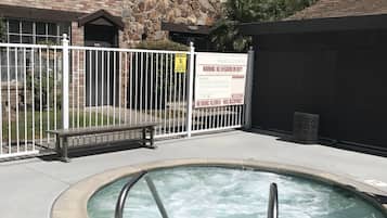 Una piscina tipo spa con una profundidad de metro y medio, rodeada por una valla blanca, con un edificio de piedra y entramado de madera al fondo.