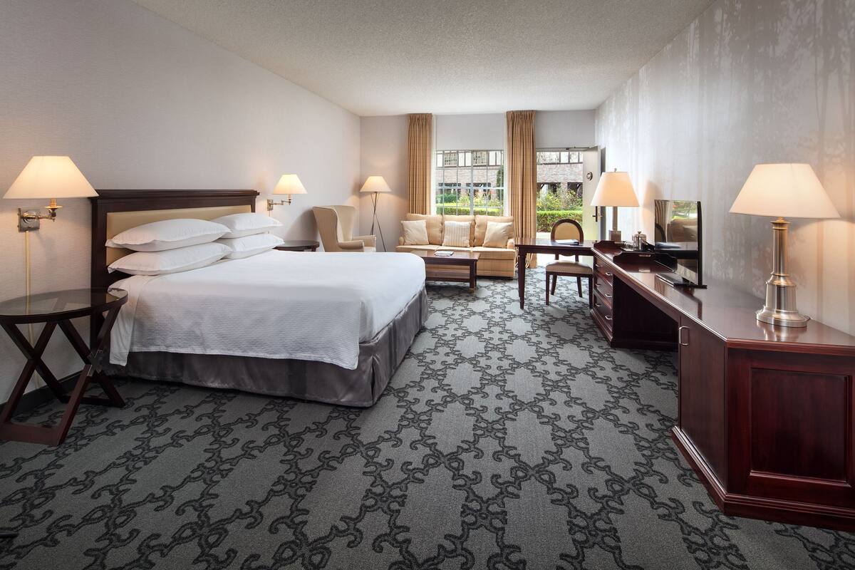 A hotel room with a large bed, two bedside tables with lamps, a sofa, a desk with a chair, and a large mirror.