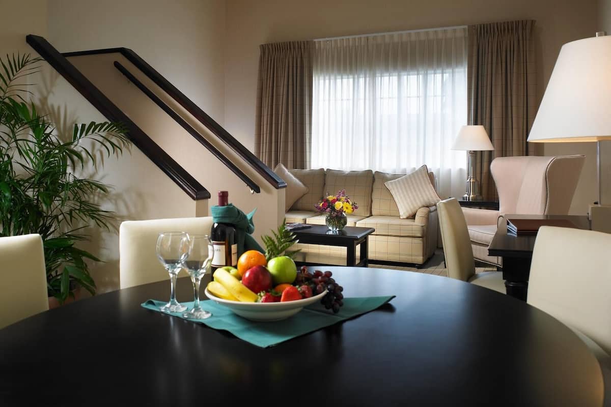 A dining area with a table set for two, a sofa, a lamp, and a staircase.