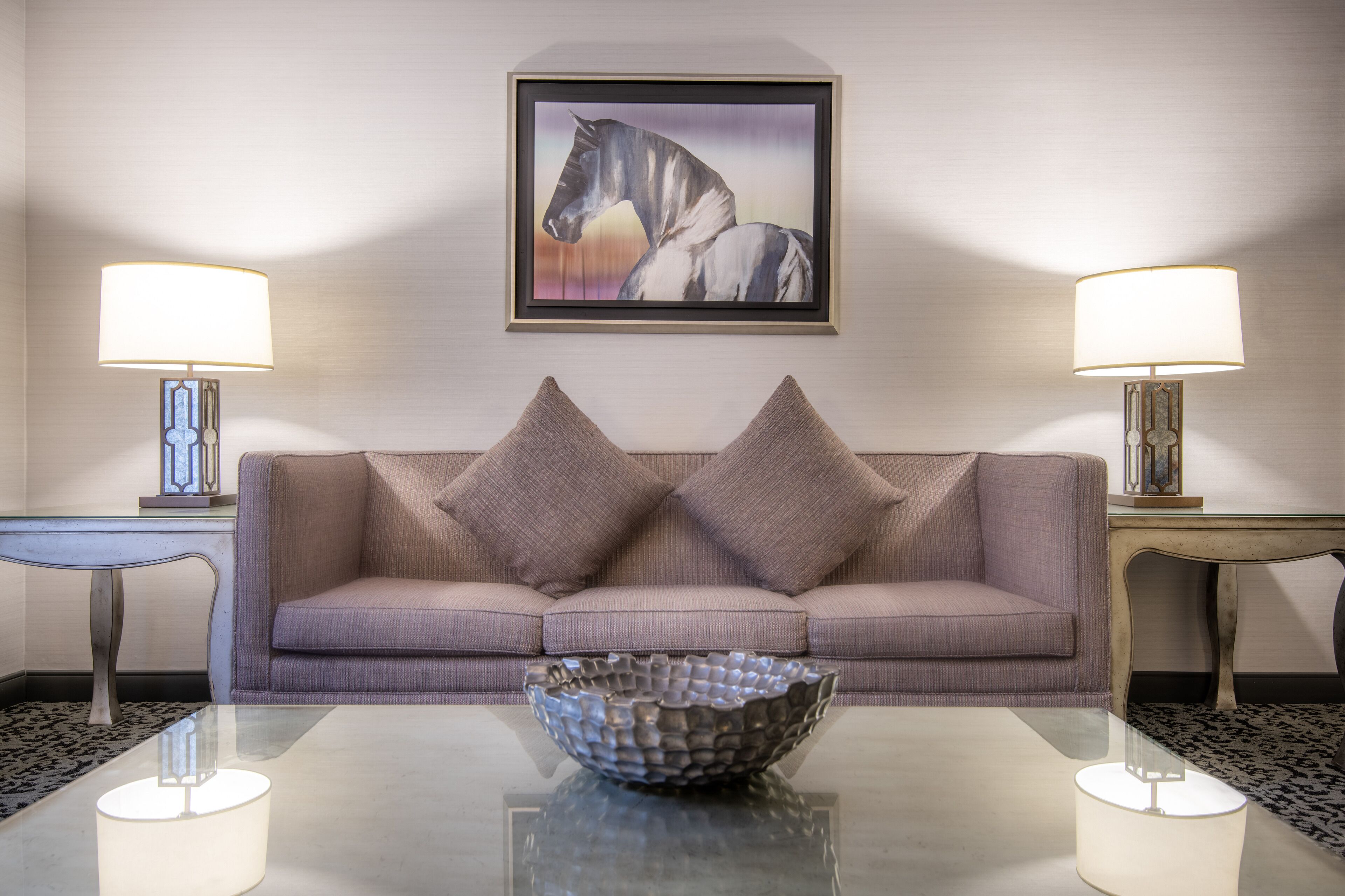 A modern living room with a sofa, two side tables, a glass coffee table, and a framed artwork on the wall.