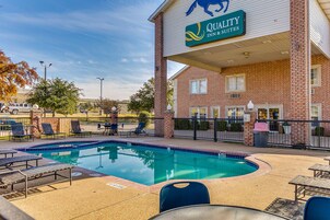 Un hotel con zona de piscina, mobiliario exterior y un cartel que dice 'Quality Inn & Suites'.