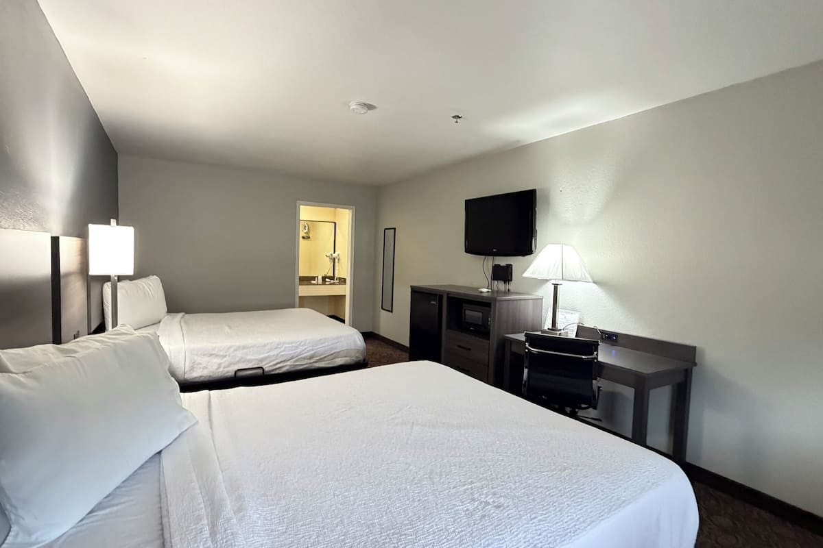 A hotel room with two beds, a desk, a chair, a TV, and a mirror.