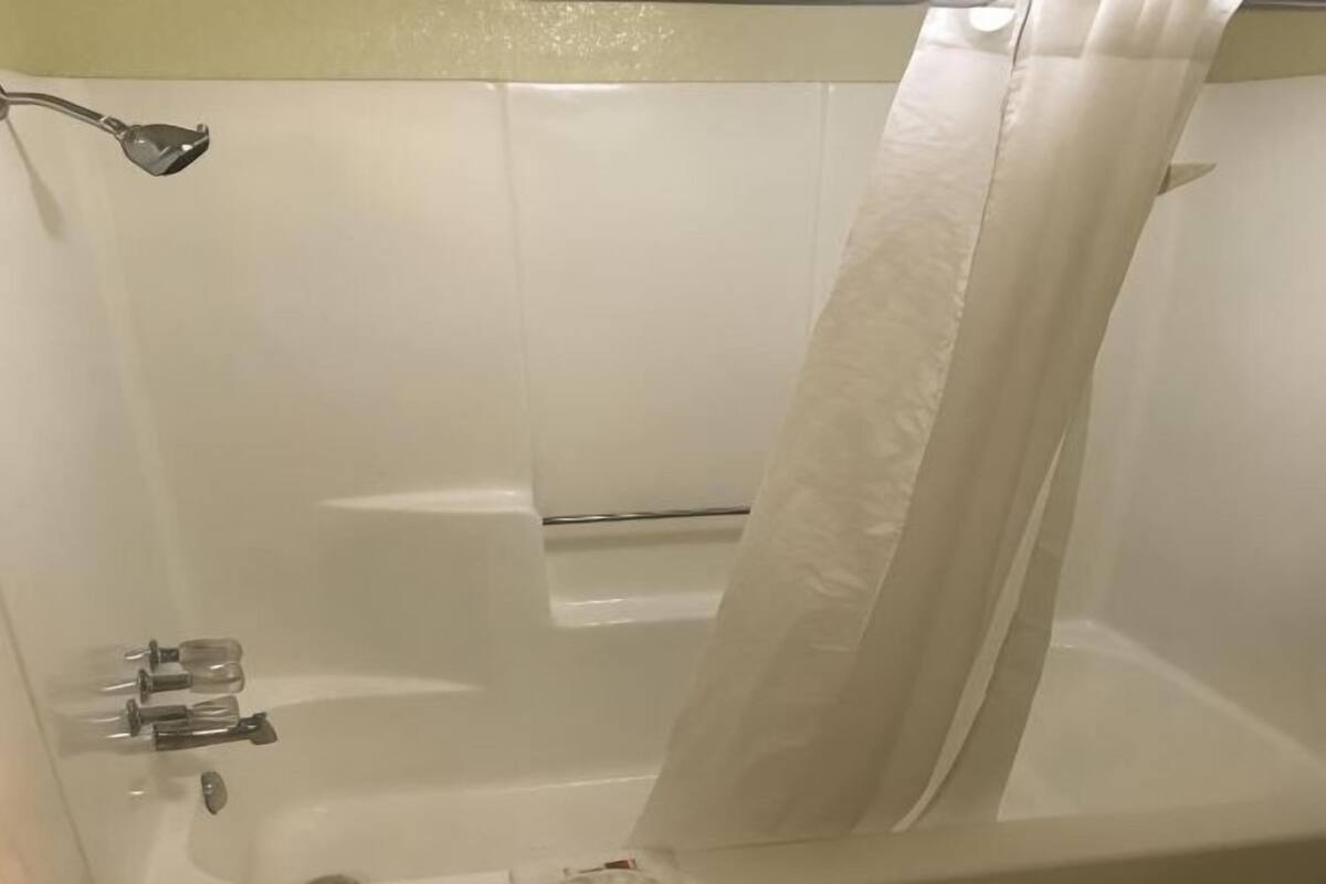 A bathtub with a shower curtain, a handheld showerhead, and a glass container.