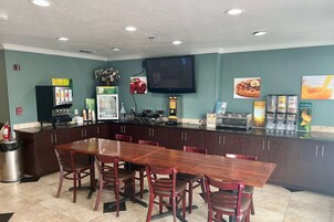 Un restaurante con una larga mesa de madera y sillas, una barra con alimentos y un televisor montado en la pared.