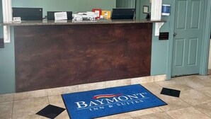 Ein Empfangsschalter mit einer blauen Matte mit der Aufschrift 'Baymont Inn & Suites' und einer Uhr an der Wand.