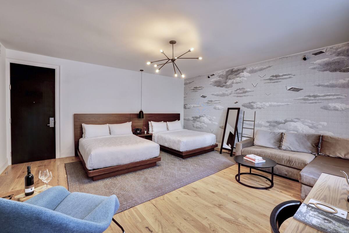 A modern hotel room with two beds, a sofa, a coffee table, and a chandelier.