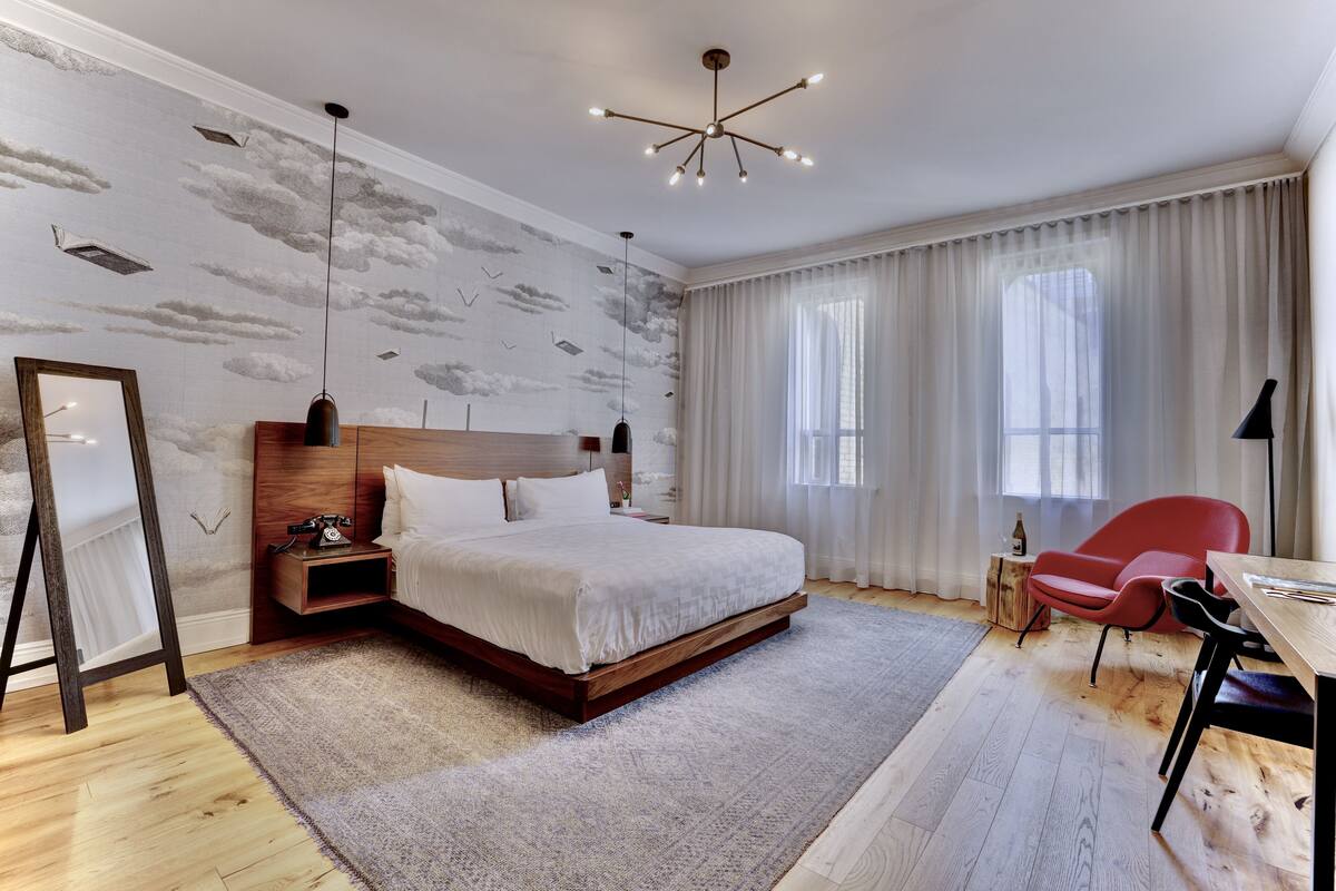 A modern bedroom with a large bed, a wooden nightstand, a red chair, and a desk with a lamp.