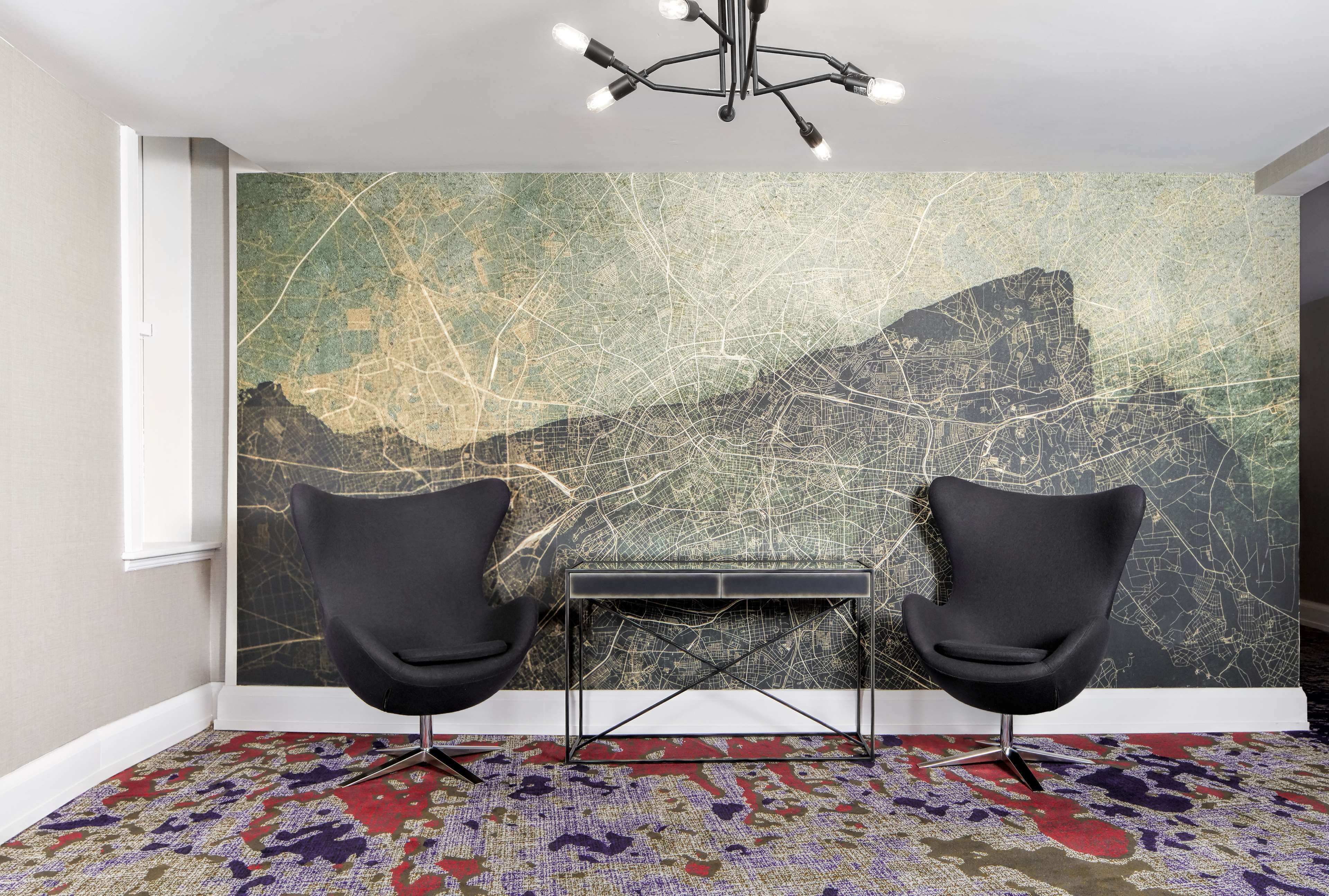 A room with a cityscape wall mural, two black chairs, a small table, and a patterned carpet.
