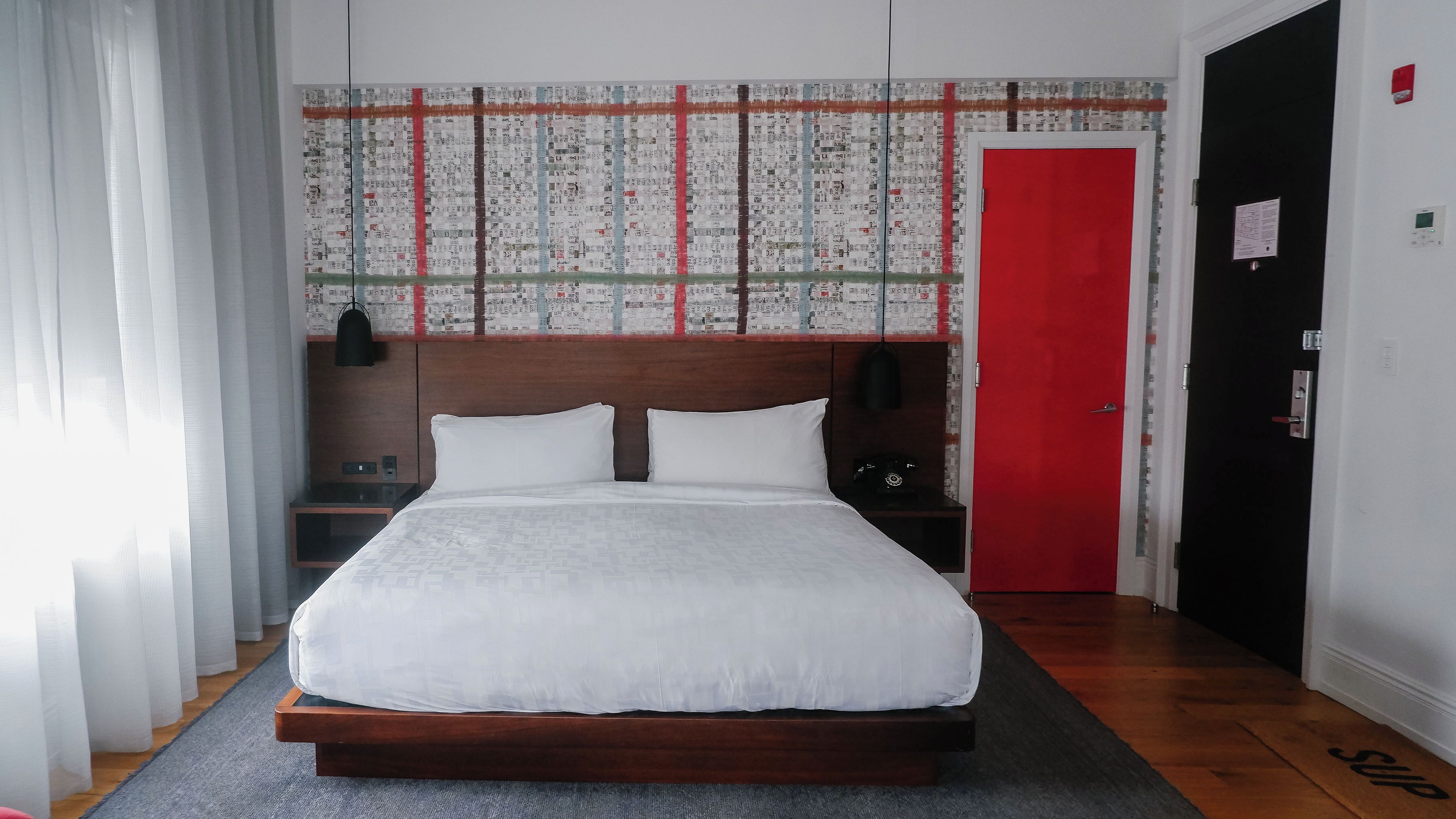 A hotel room with a large bed, wooden headboard, and a red door.