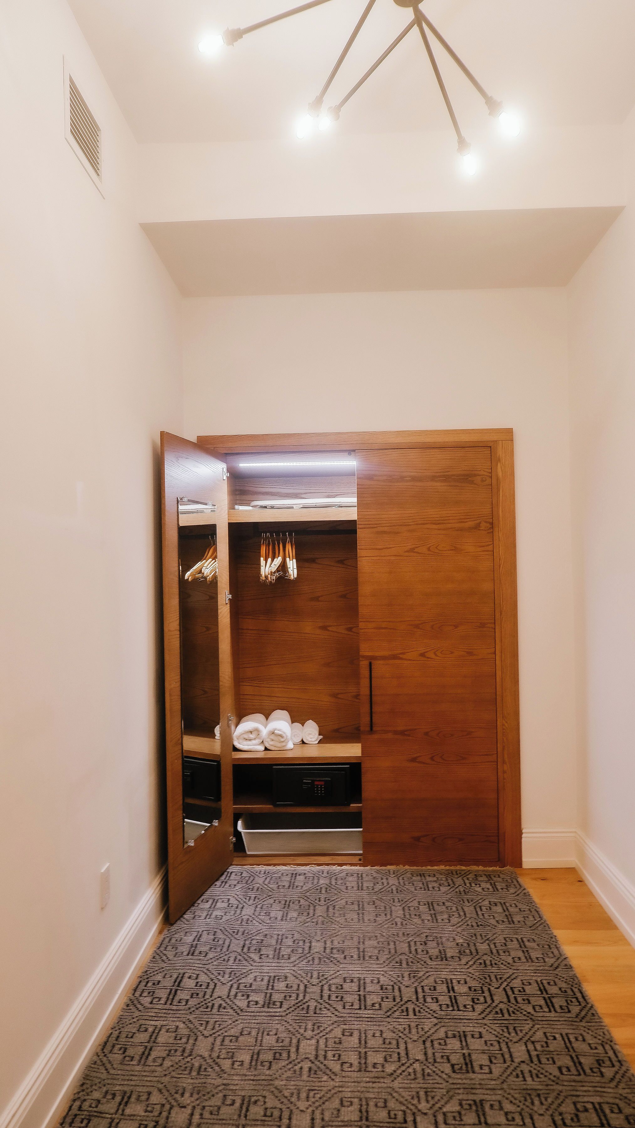 A walk-in closet with wooden doors, a built-in heater, and a patterned rug on the floor.