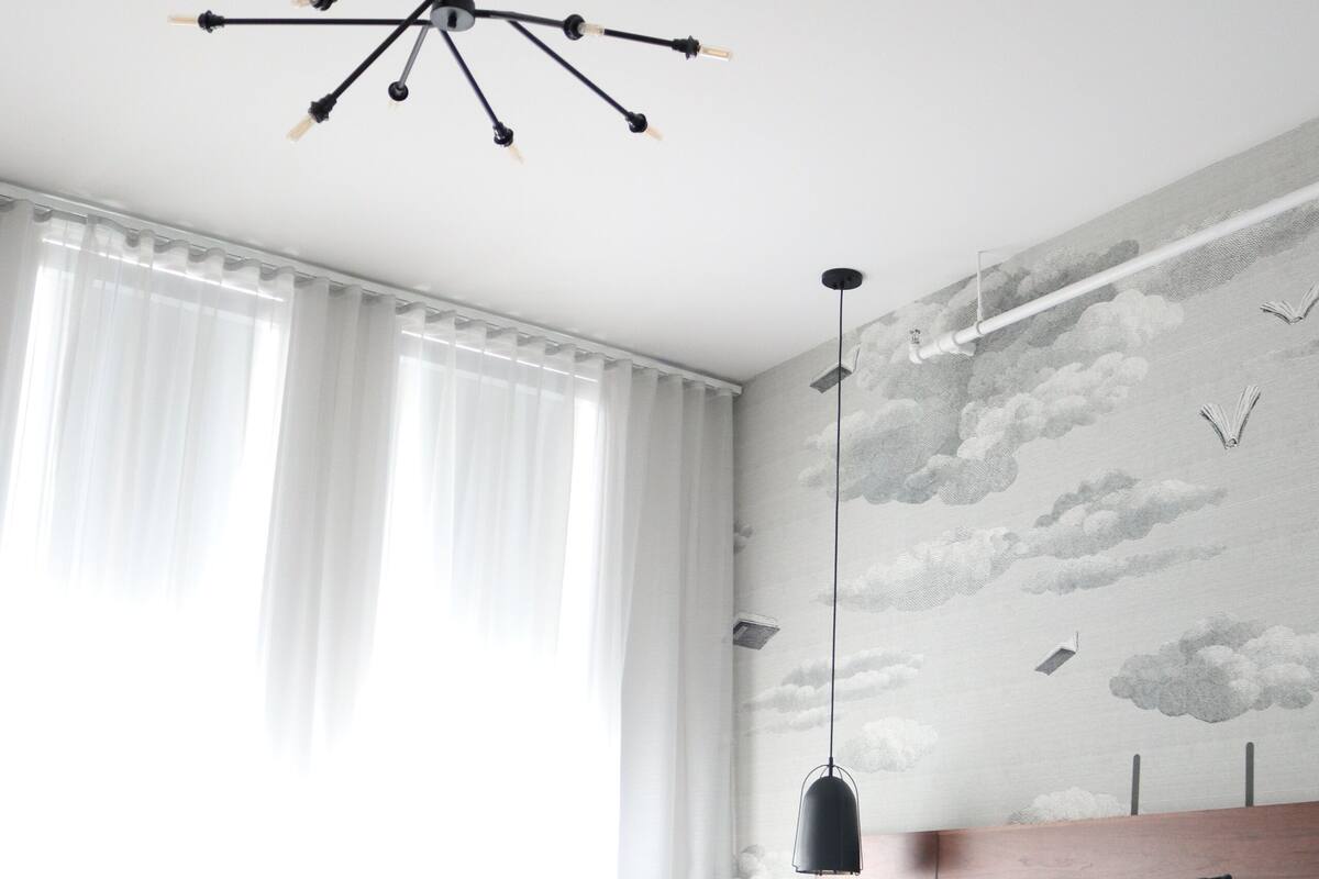 A modern bedroom with a large bed, a unique ceiling light fixture, and a wall mural.