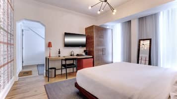 A modern hotel room with a large bed, a desk with a chair, a television, and a wardrobe.