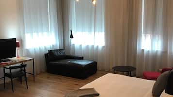 A modern hotel room with a large bed, a desk with a chair, a black leather sofa, and a small table.
