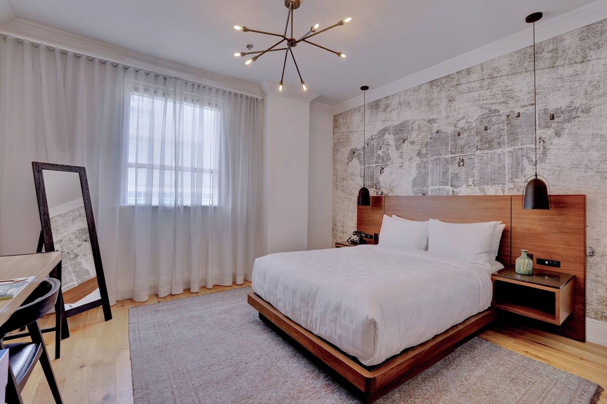 A modern bedroom with a large bed, wooden headboard, and a cityscape mural on the wall.