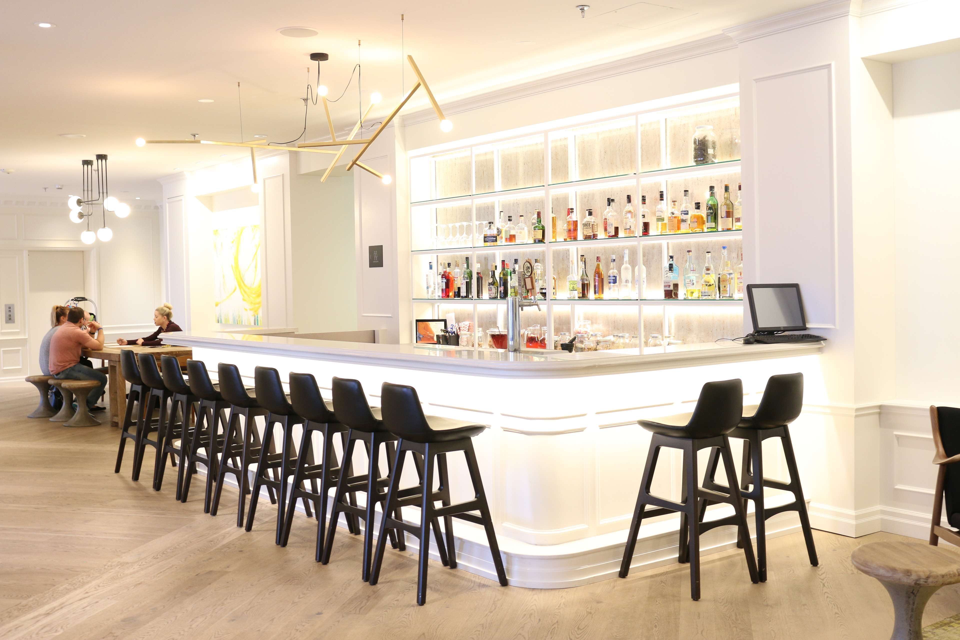 Uma área de bar com um balcão comprido, vários bancos e interior bem iluminado.