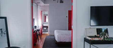 A hotel room with a bed, a desk, a chair, a TV, and a painting on the wall.