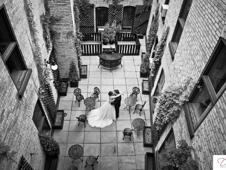 A courtyard with a bride and groom dancing, surrounded by brick buildings and outdoor furniture.