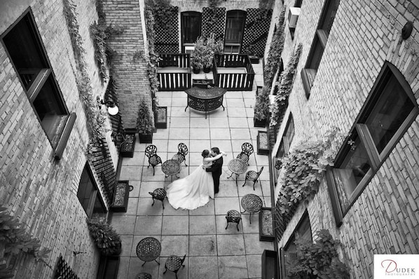 Courtyard with a central seating area and potted plants, surrounded by brick walls with climbing plants.