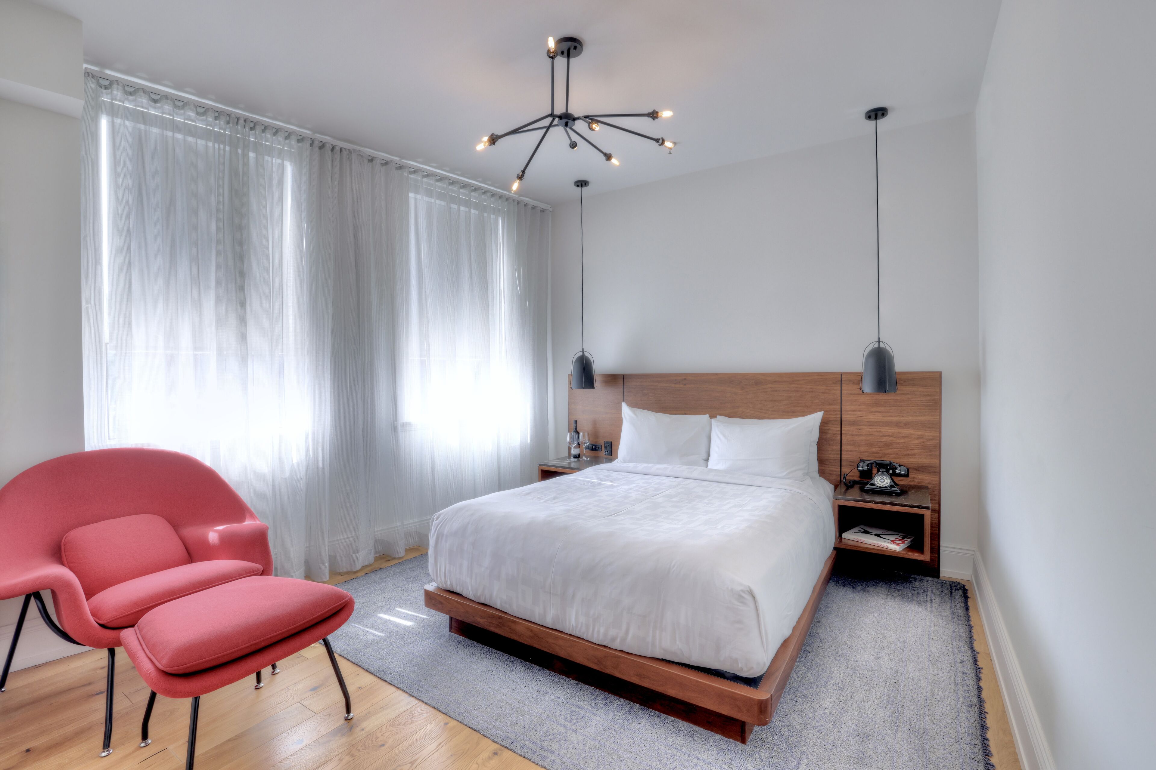 A modern bedroom with a large bed, a red chair, a wooden headboard, and two pendant lights.