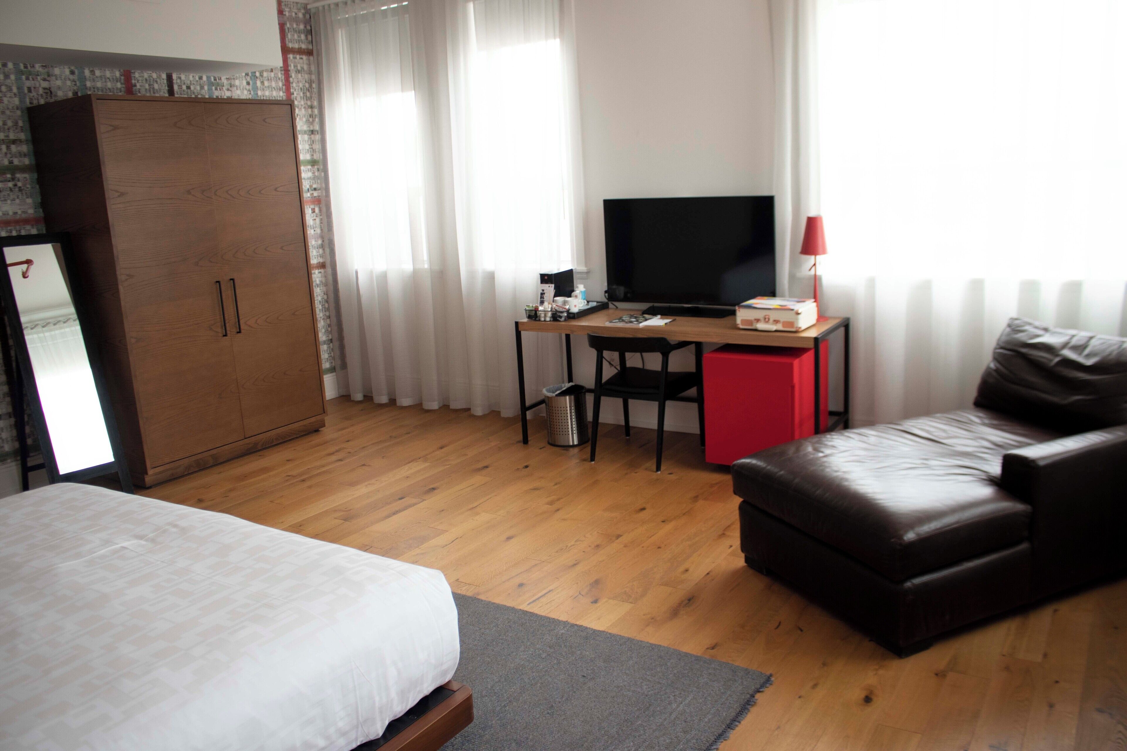A hotel room with a bed, a desk with a TV, a red cabinet, and a leather sofa.