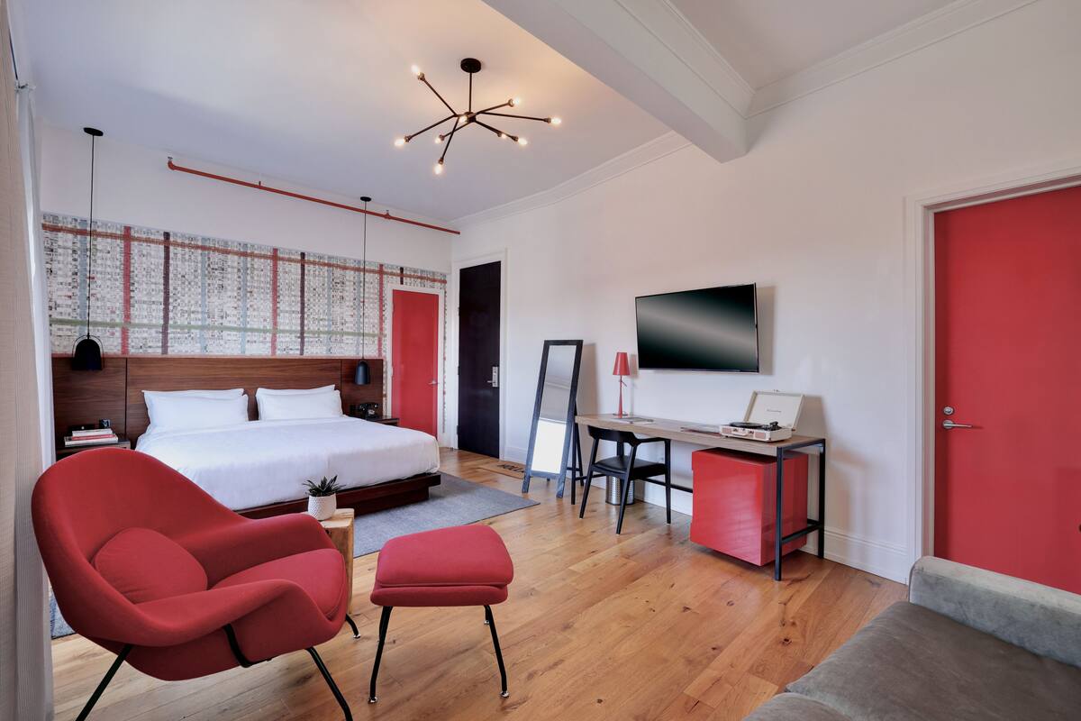 A modern bedroom with a bed, a desk, a red chair, and a TV.