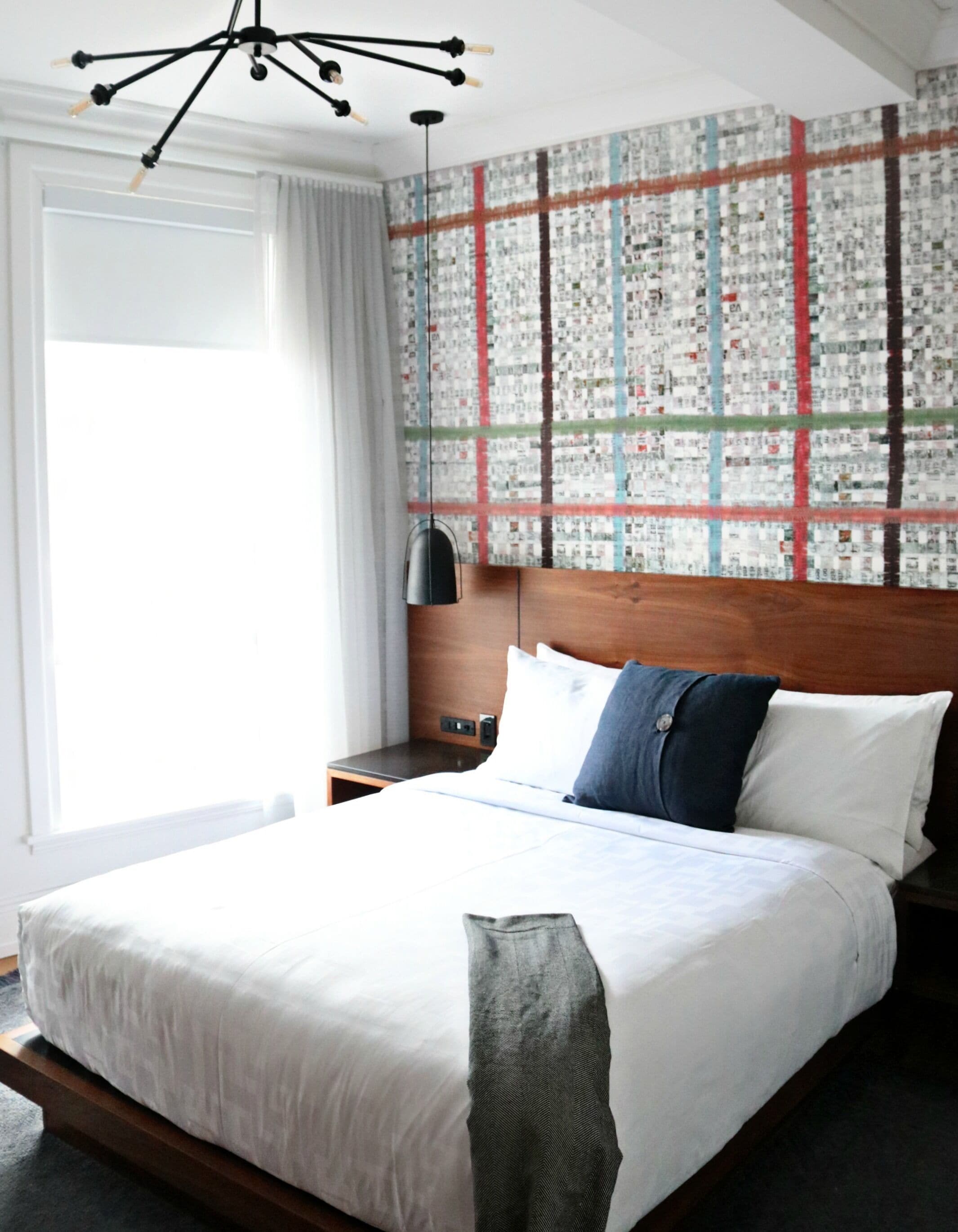 A hotel room with a large bed, a wooden headboard, a wall art piece, a nightstand, and a modern chandelier.