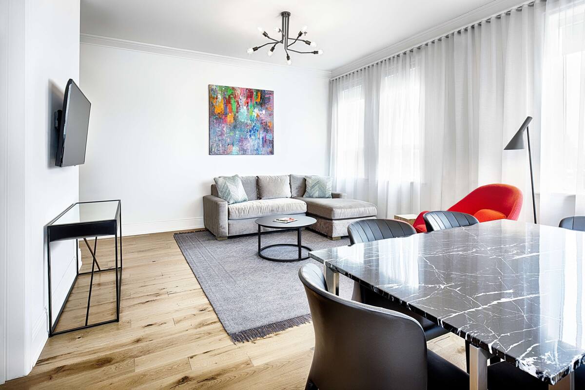 A modern living room with a sofa, a coffee table, a dining table, and a TV mounted on the wall.