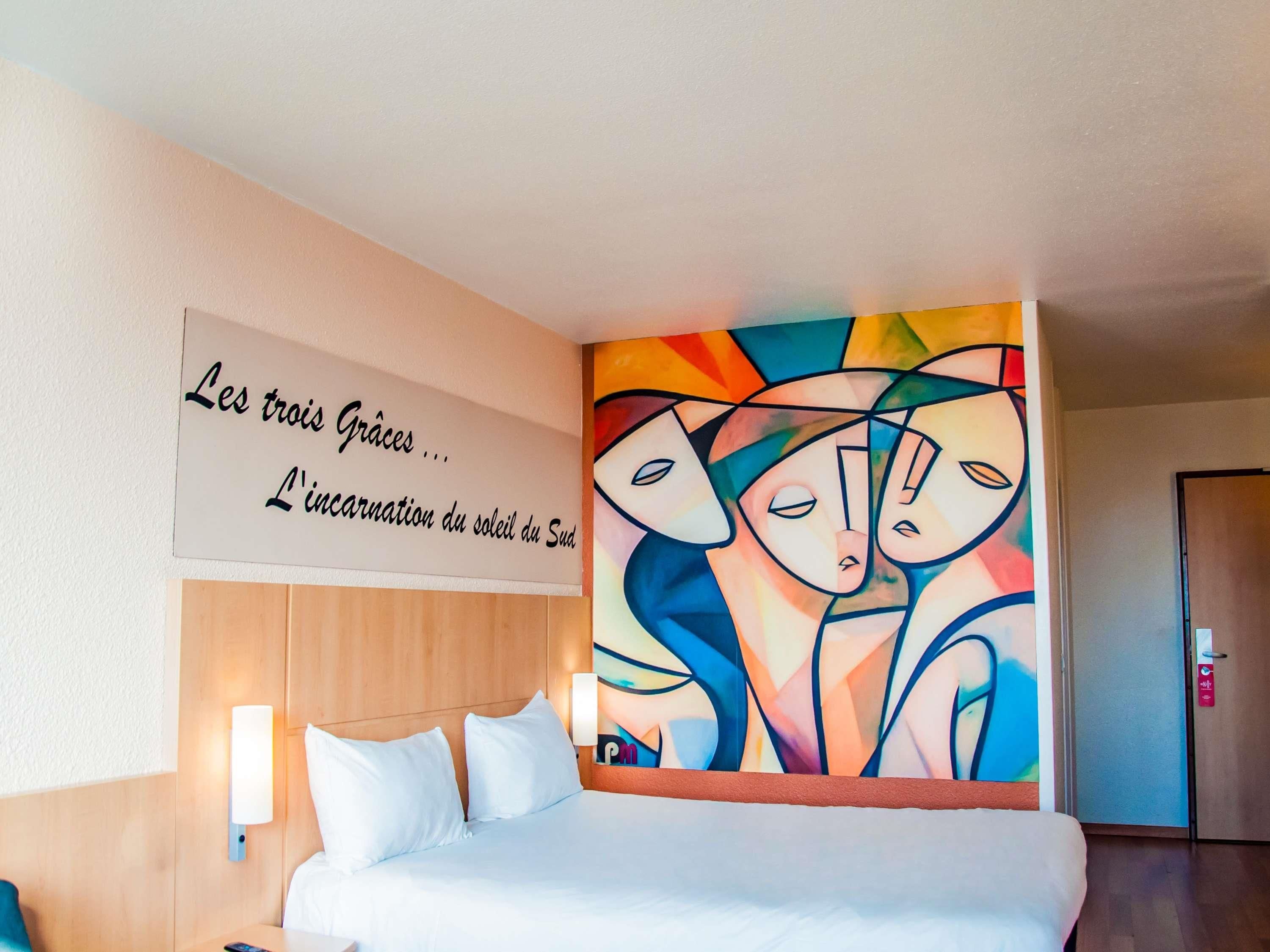 Ein Hotelzimmer mit einem Bett, einem an der Wand befestigten Schild und einem farbenfrohen abstrakten Gemälde.