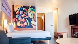 A hotel room with a bed, a painting on the wall, a television, and a small table. - ibis Montpellier Centre Comédie (Montpellier)