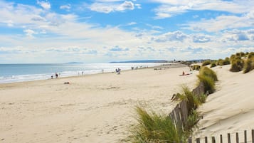 A sandy beach with a wooden fence and dunes, a clear sky, and distant hills.