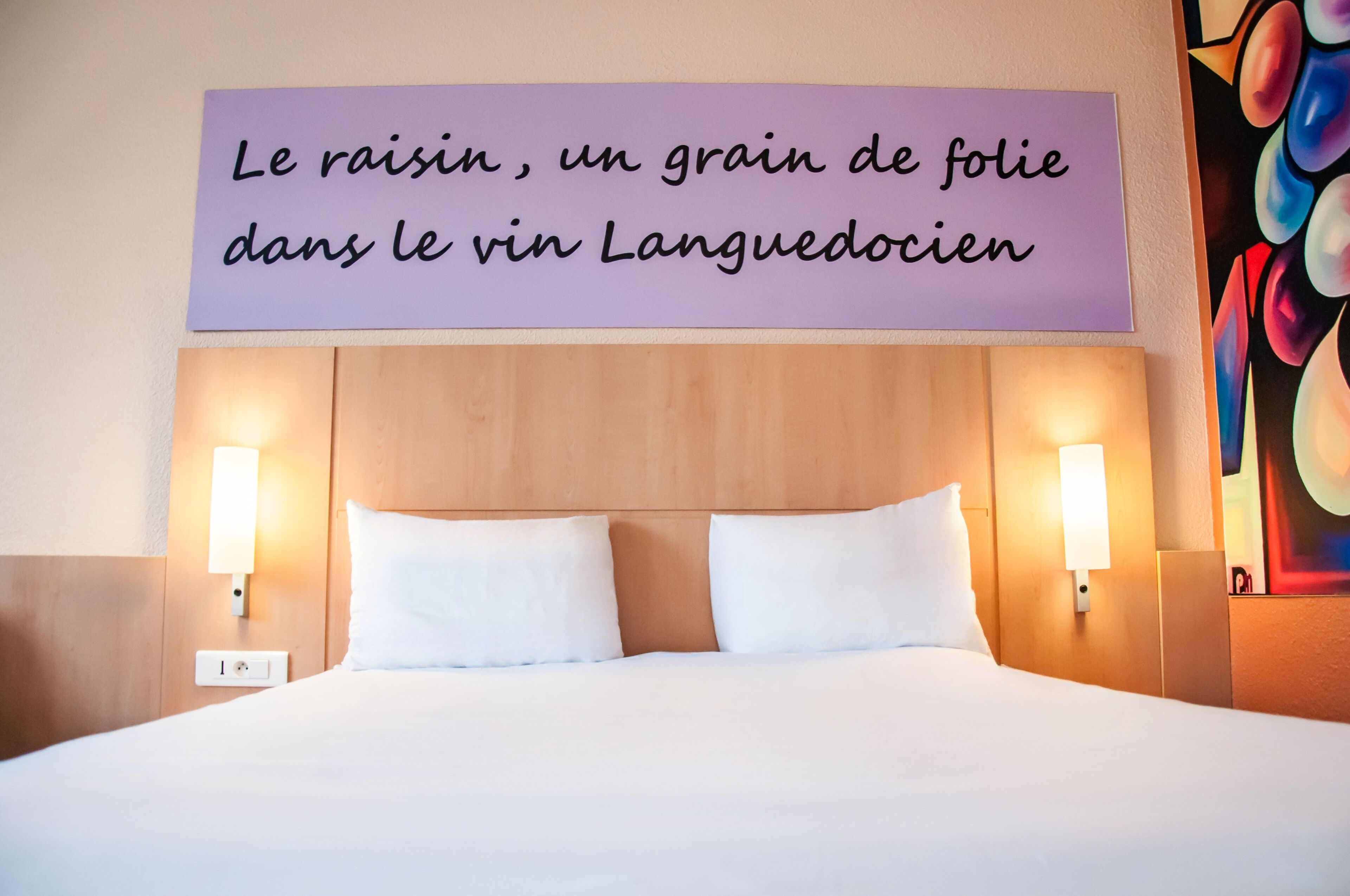 Et hotelværelse med en seng, to sengeborde med lamper og en væg med et skilt på fransk.