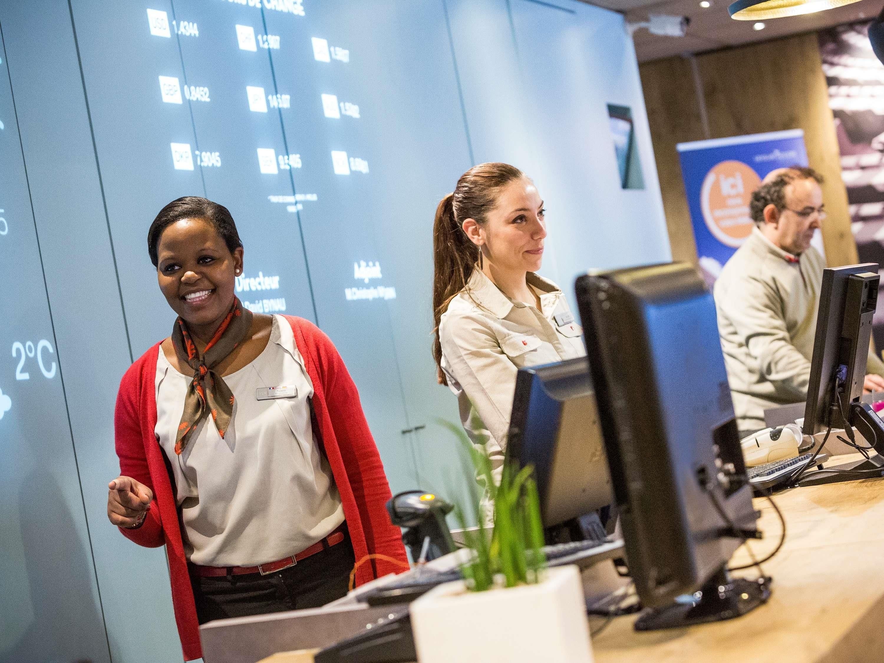 A reception area with a digital display showing currency exchange rates, a reception desk, and a computer monitor.