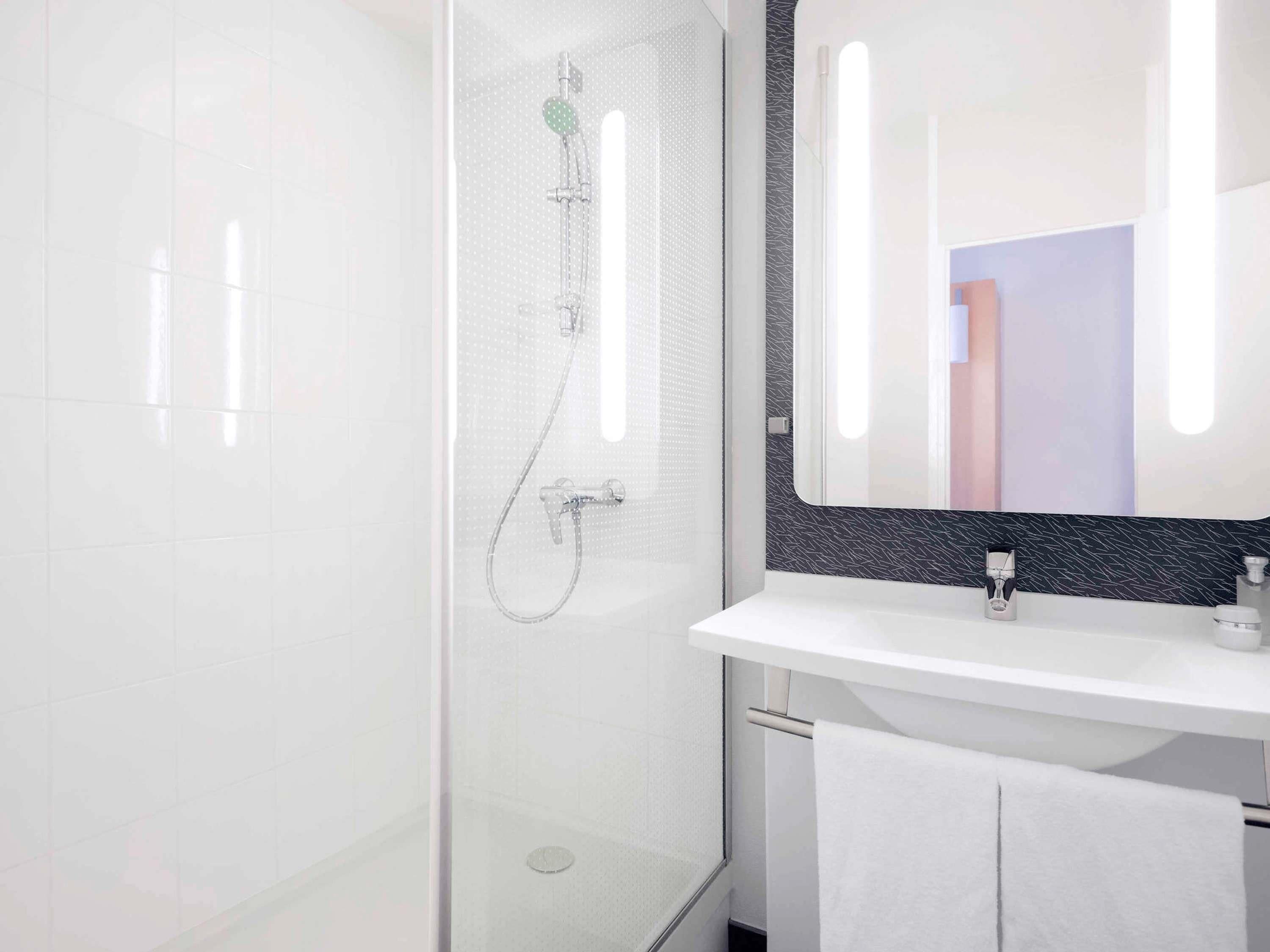 A modern bathroom with a glass shower enclosure, a white sink, and a mirror with a black backsplash.