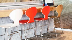 A reception area with a wooden counter, a black digital display, and four modern chairs with metal frames and red cushions. - ibis Montpellier Centre Comédie (Montpellier)