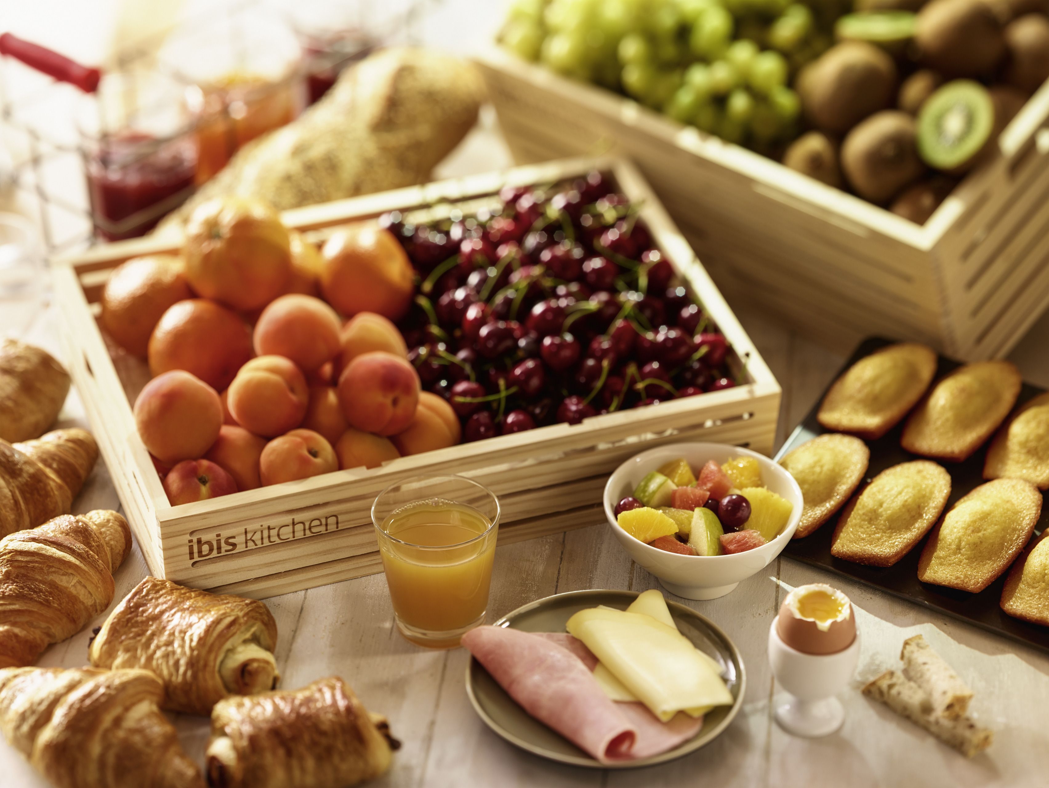 Una mesa con frutas, bollería y un vaso de zumo de naranja.