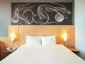 Una habitación de hotel con una cama grande, dos lámparas de noche, un cabecero de madera y una obra de arte en la pared sobre la cama.